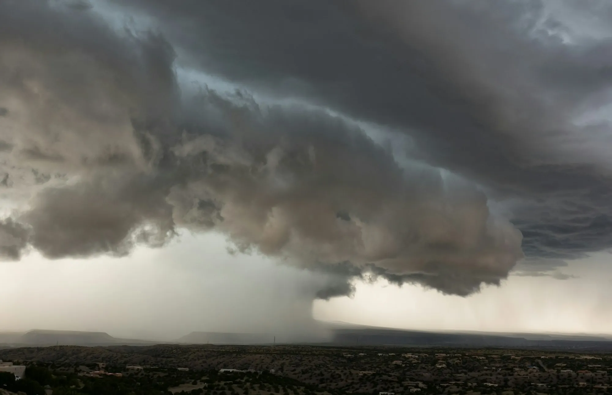 Massive shelf cloud with rain falling over a town, the kind of storm that leaves roof damage to photograph for an insurance claim in Mableton