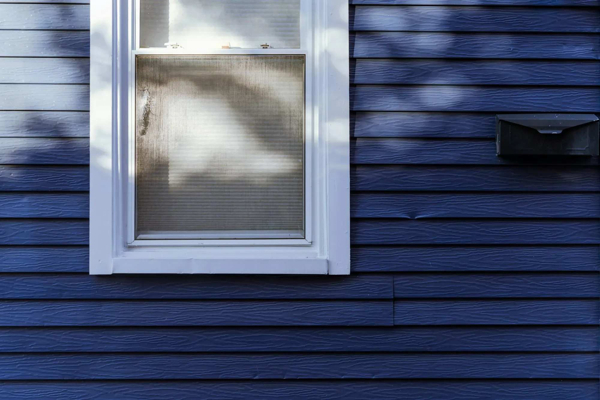 Navy blue lap siding around a white-trimmed window